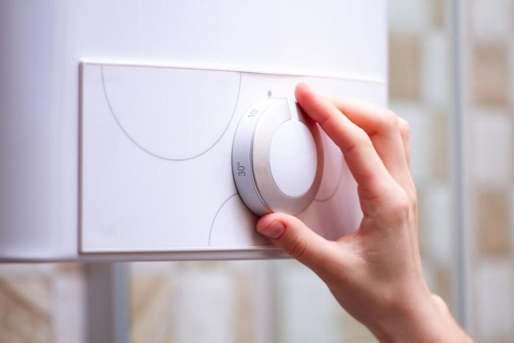 Hand adjusting a white smart thermostat dial set to 30 degrees on a wall near a sunny window.