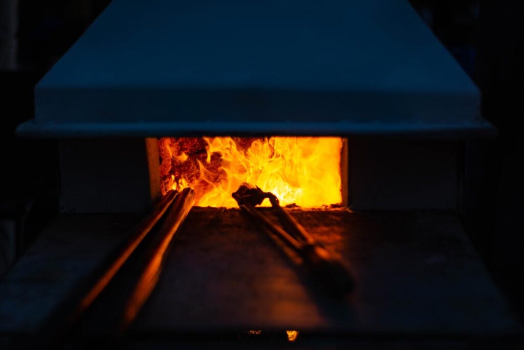 Industrial furnace with glowing orange flames visible through glass viewing window and metal rods extending into the chamber.