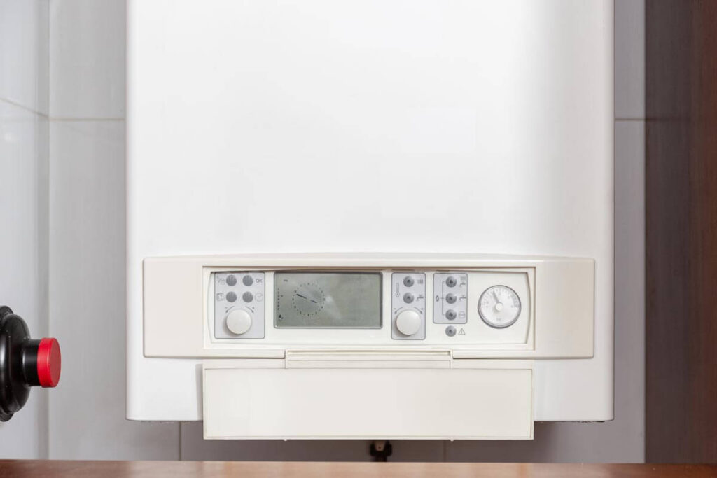 Wall-mounted white tankless water heater control panel with digital display, temperature controls, and analog dial gauge.