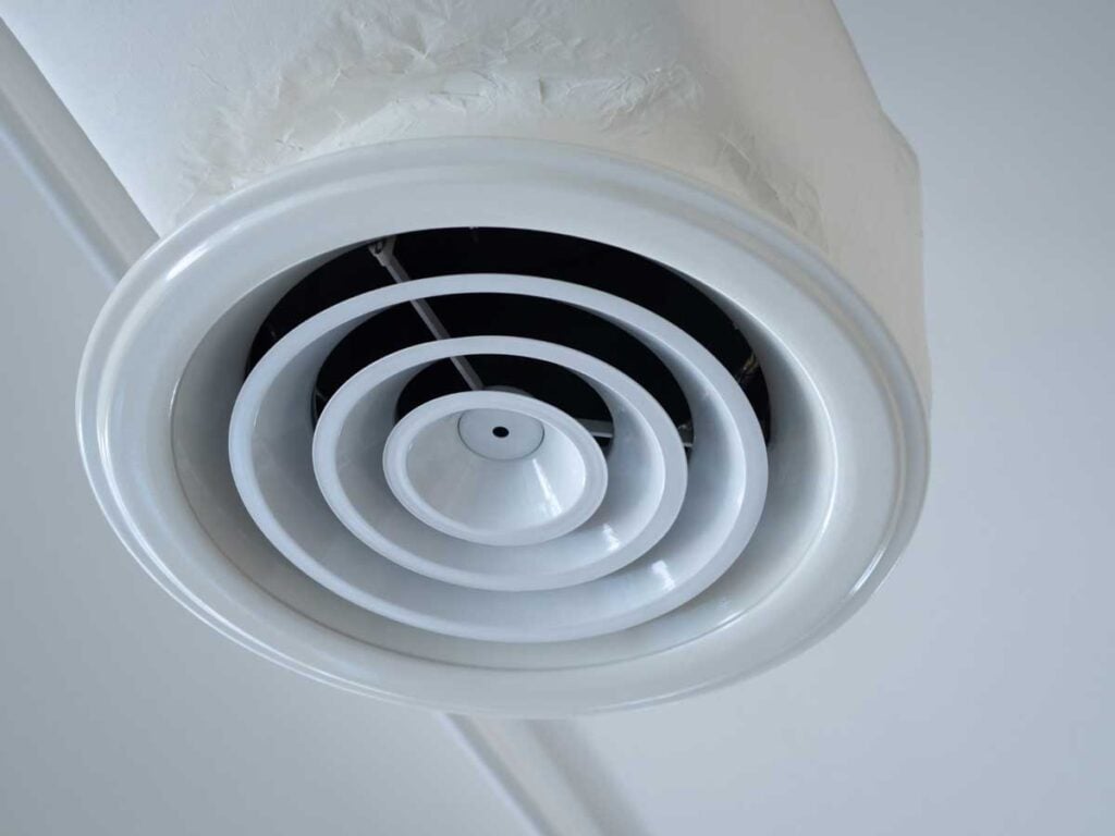 White ceiling-mounted round air duct vent with concentric rings showing moisture and condensation accumulation on the surface.