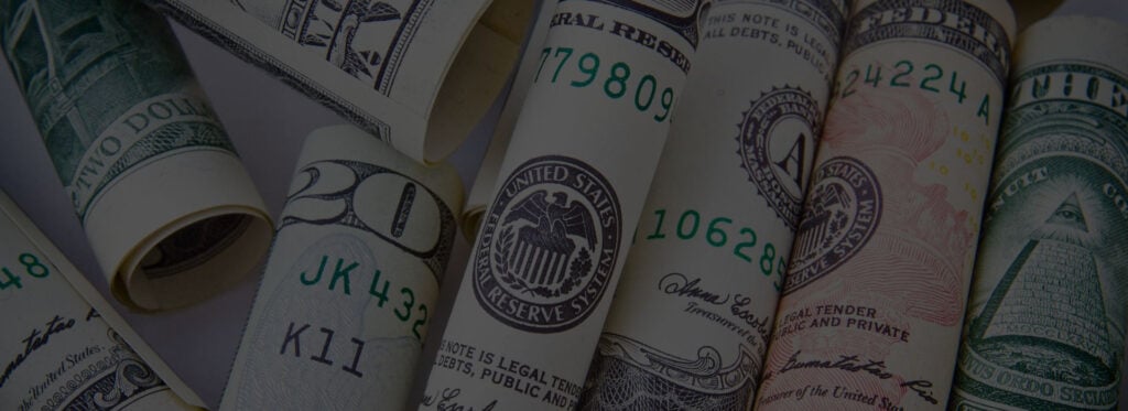 Rolled US currency bills displaying Federal Reserve seals, serial numbers including 17809, 10628, and 24224, with visible text stating legal tender.