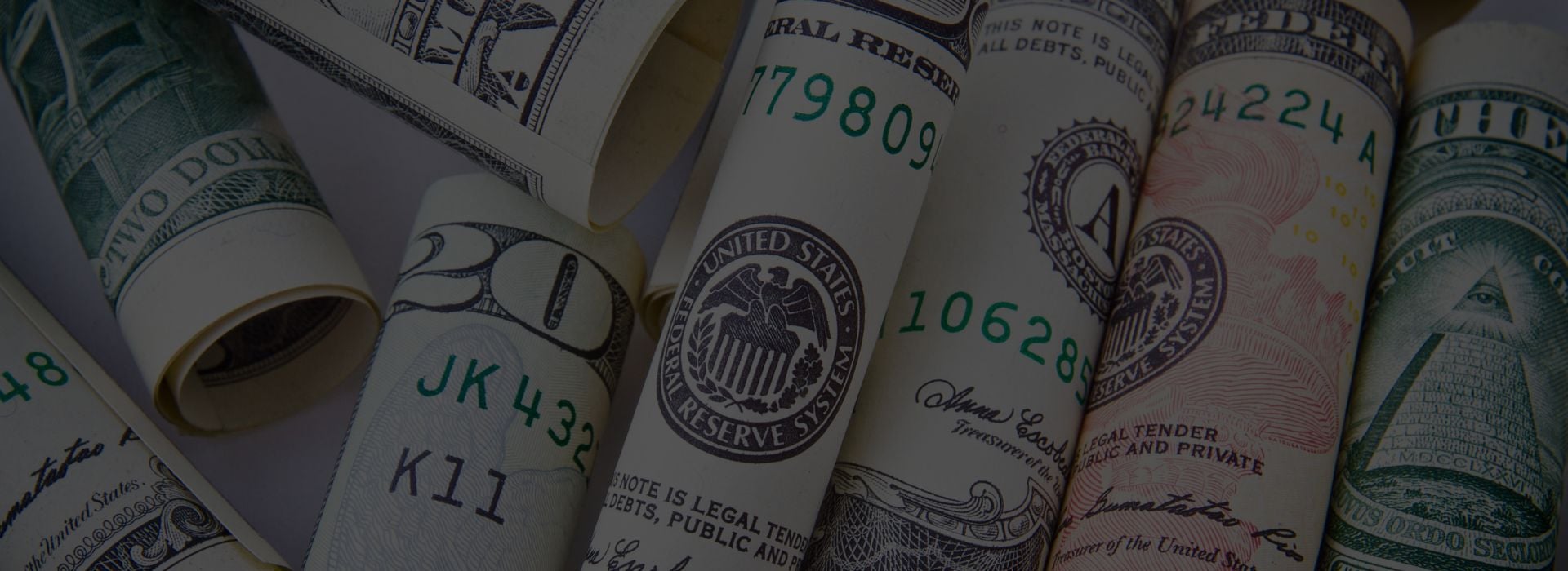 Rolled US currency bills displaying Federal Reserve seals, serial numbers including 17809, 10628, and 24224, with visible text stating legal tender.