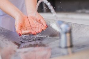 Person cupping hands under a stream of flowing water from a faucet, demonstrating proper handwashing hygiene and clean water access.
