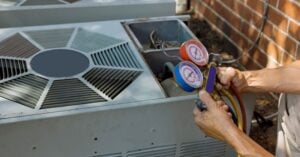 Technician holding pressure gauges connected to an air conditioning unit for refrigerant level inspection and maintenance.