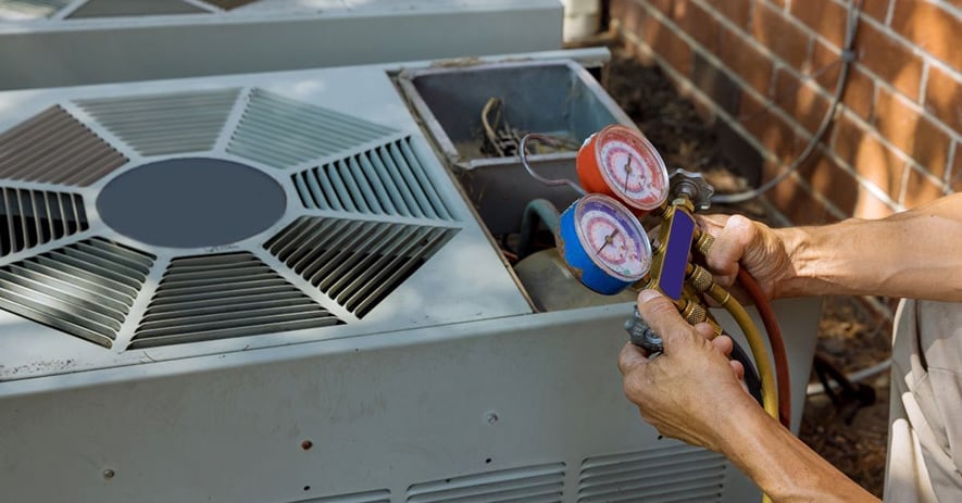 Technician holding pressure gauges connected to an air conditioning unit for refrigerant level inspection and maintenance.