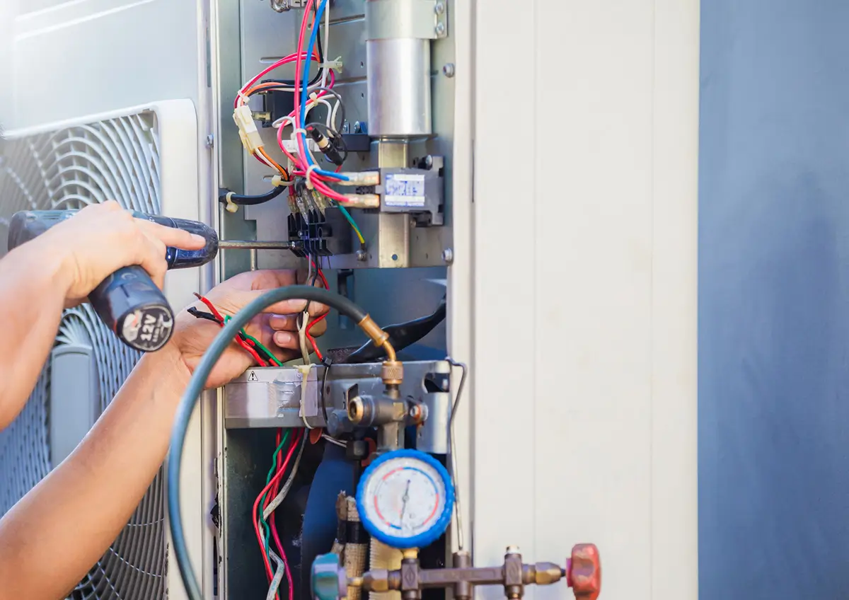 HVAC technician using digital multimeter to test air conditioning system internal components and refrigerant gauge.