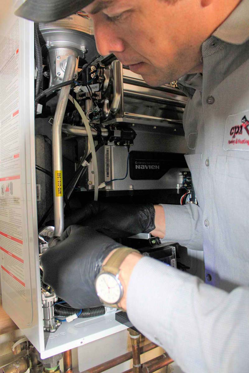 HVAC technician in black gloves installs Navien heating unit components during furnace maintenance or installation work.