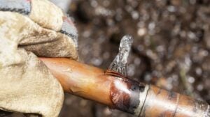 Close-up of a gloved hand using a soldering torch to heat and join copper pipes during plumbing repair work.