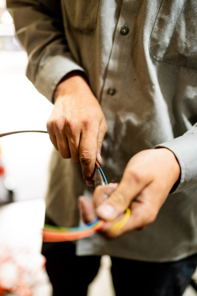 Electrician in khaki work shirt using a wire stripping tool on multicolored electrical wires.